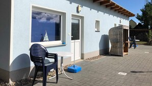 Un edificio de color azul claro, con vigas de madera en el techo, una ventana con un modelo de velero, una puerta y una pequeña mesa con una silla en el exterior.