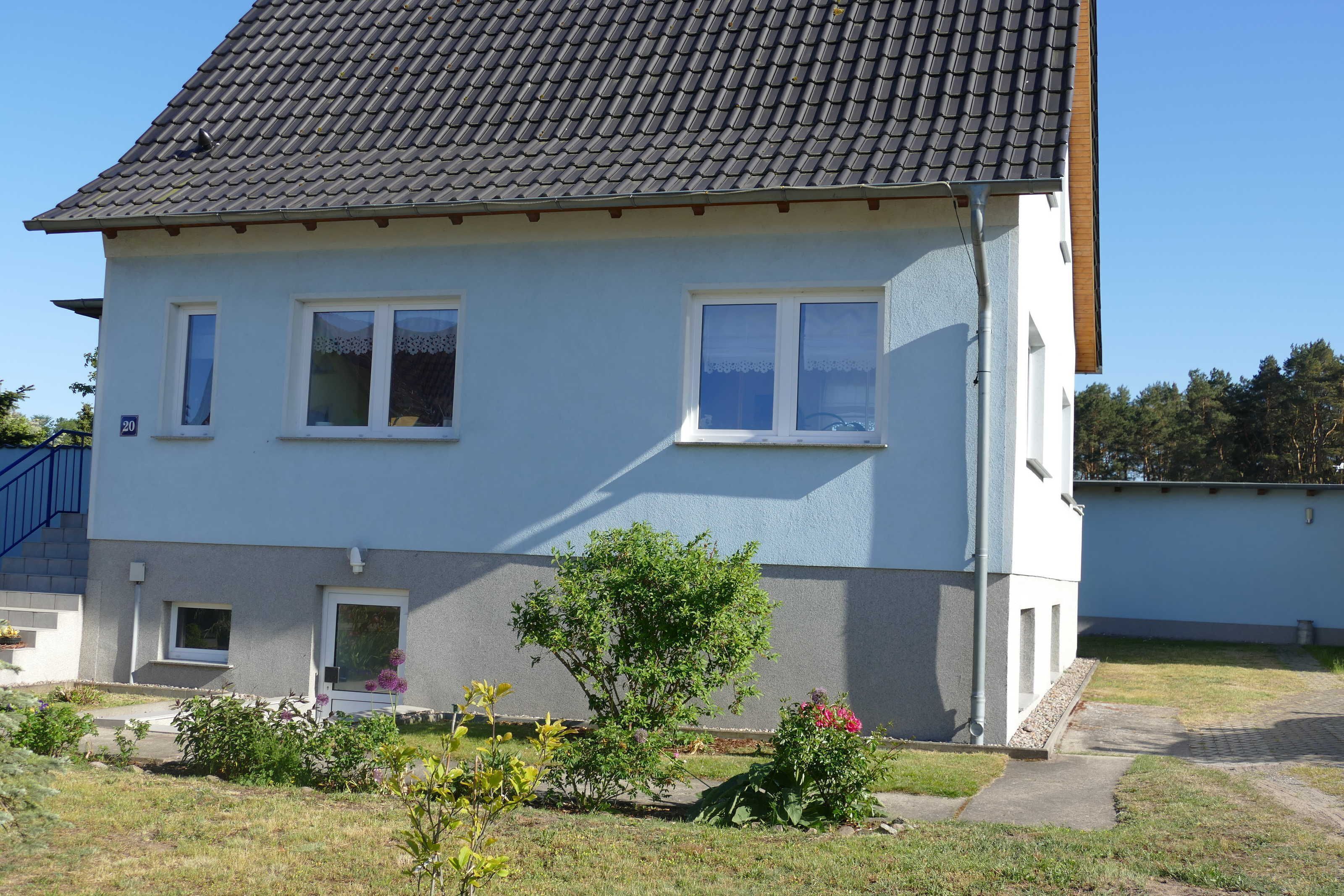Ein zweistöckiges Haus mit Ziegeldach, einer kleinen Veranda und einem Garten mit verschiedenen Pflanzen und Blumen.