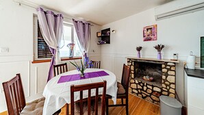 Een eetgedeelte met een stenen open haard, een witte tafel met een paarse tafelkleed en houten stoelen.