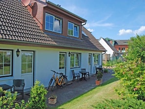 A two-story house with a tiled roof, a patio with outdoor furniture, and a bicycle parked outside.