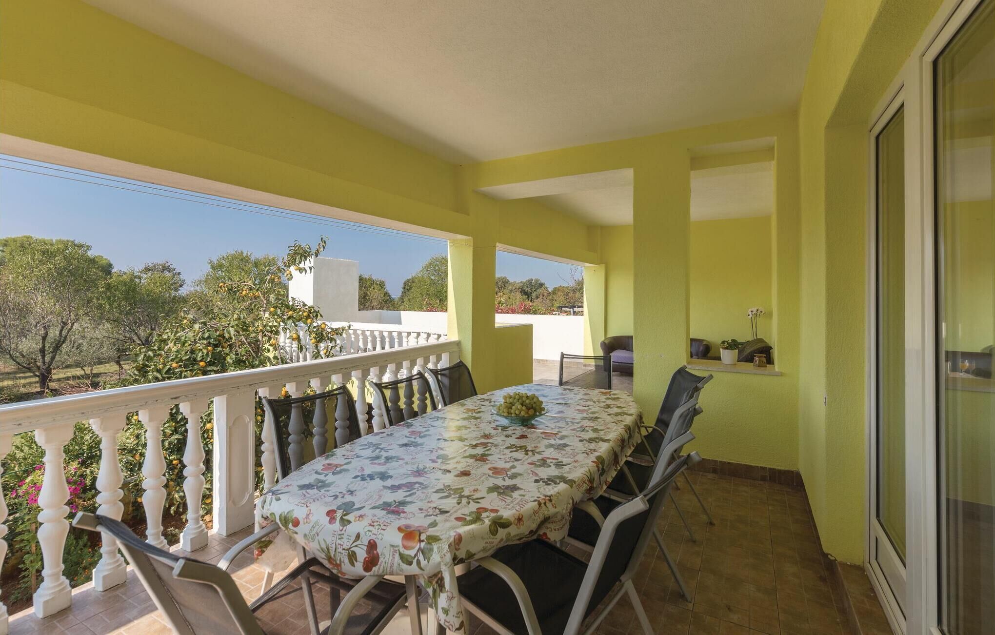 A balcony with a table and chairs, a potted plant, and a view of trees and buildings.