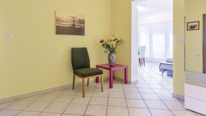 Una habitación con una silla verde, una mesita con un florero y un cuadro en la pared.