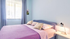 Un dormitorio con cama, mesita de noche, lámpara y ventana con cortinas.