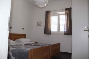 Ein Schlafzimmer mit einem hölzernen Bett, einem Fenster mit Vorhängen, einem kleinen gerahmten Bild an der Wand und einer Deckenleuchte.