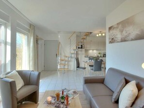 A modern living room with a sofa, a coffee table, and a dining area in the background.