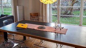 Un coin repas avec une table dressée pour deux personnes, une chaise, une lampe et une vue sur l’extérieur.