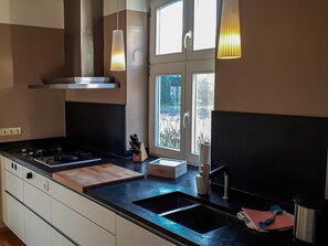 A modern kitchen with a black countertop, stainless steel sink, and a window with a view of greenery.