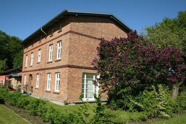 A brick building with a symmetrical facade, large windows, and a well-maintained garden with flowering shrubs.