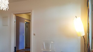 Une pièce comprenant une chaise transparente, une petite table, une lampe et une porte donnant sur une autre pièce.