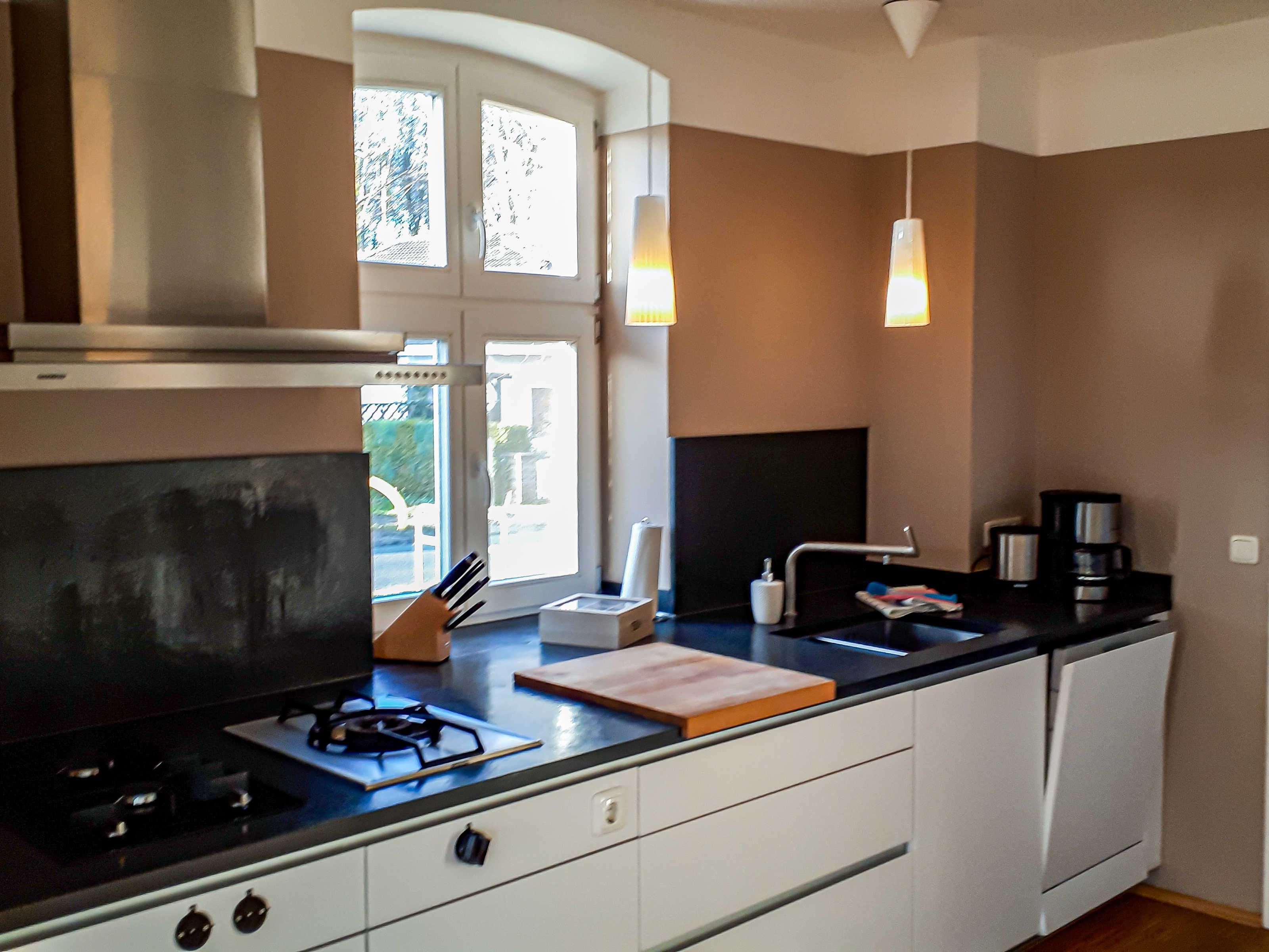 A modern kitchen with a gas stove, white cabinets, a black countertop, and a window with natural light.