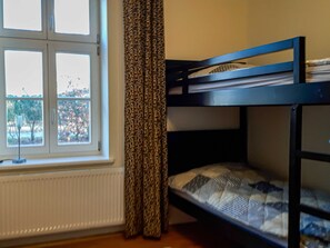 A bunk bed with a window and curtains, a radiator, and a view of a cityscape.