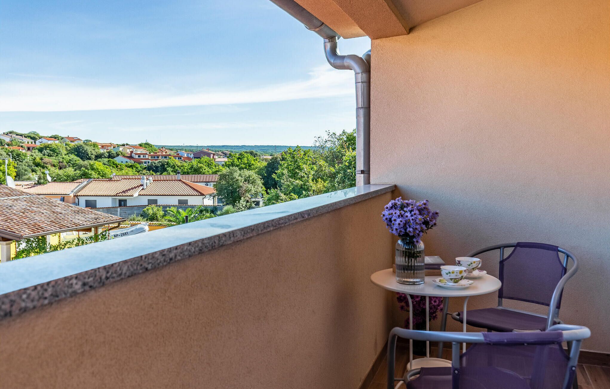 Un balcon donnant sur un quartier résidentiel, une petite table avec un vase de fleurs et deux chaises.