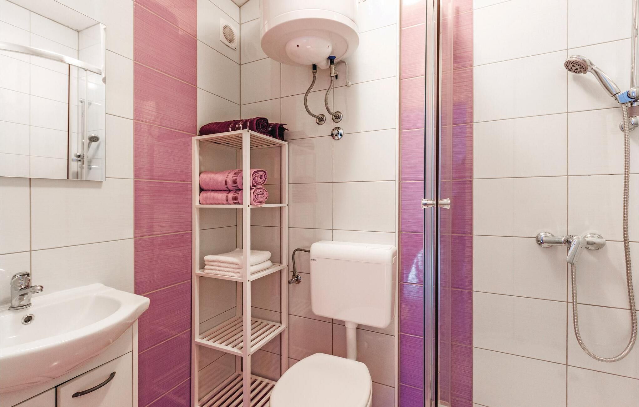 Une salle de bain avec un lavabo blanc, des toilettes, une douche avec un pommeau de douche amovible et une étagère avec des serviettes pliées.
