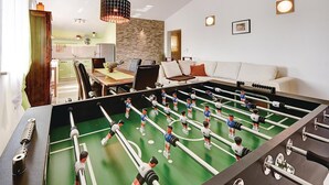 A room with a foosball table, a sofa, and a kitchen area in the background.