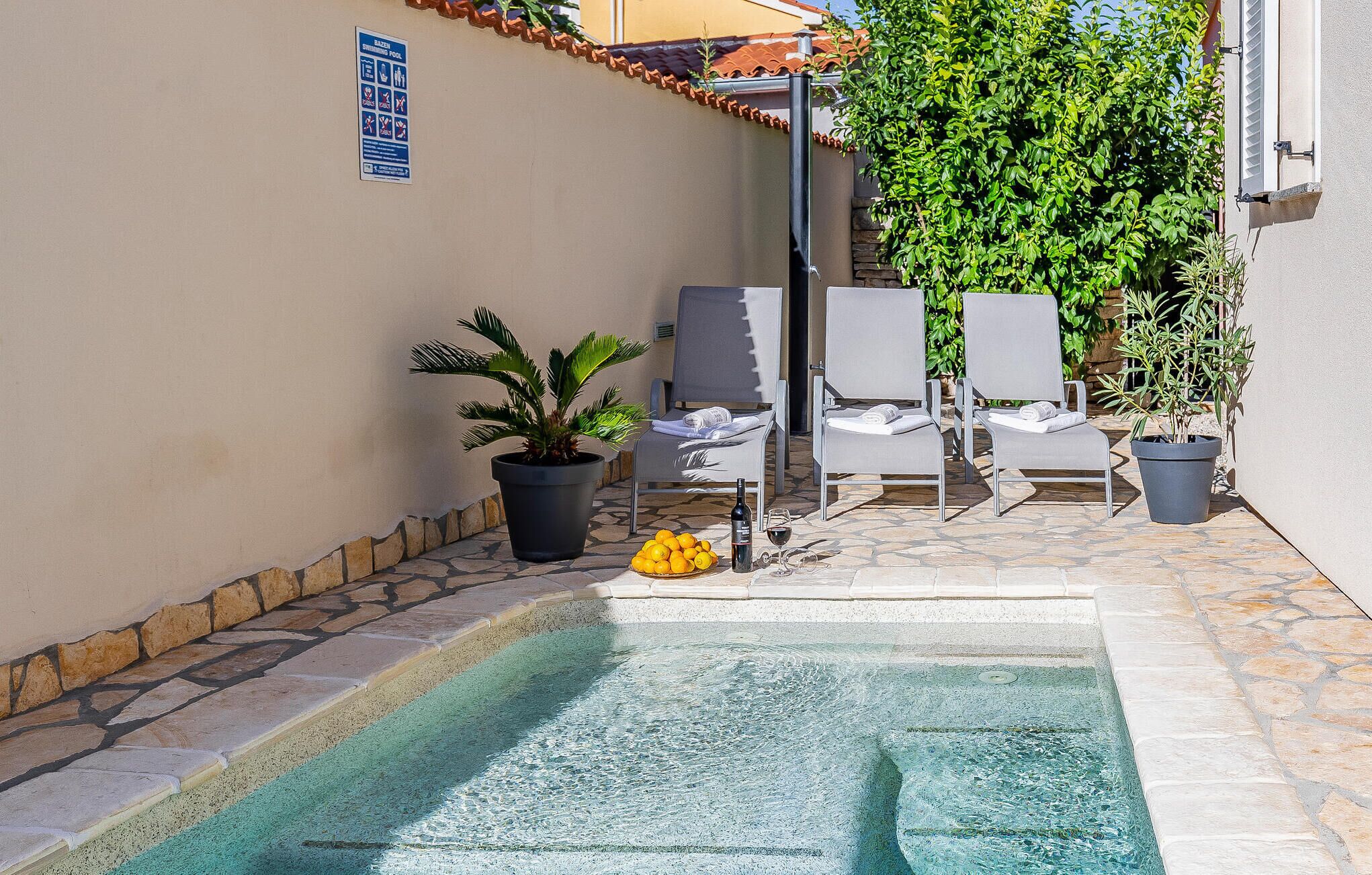 A pool area with lounge chairs, a potted plant, and a sign indicating a swimming pool.