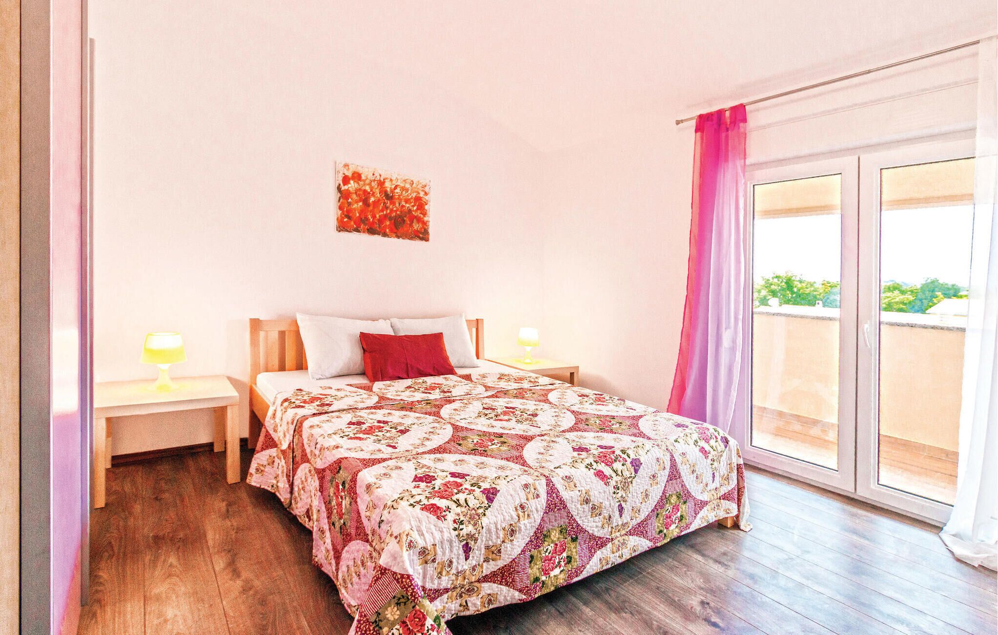 Un dormitorio con una cama grande, dos mesitas de noche, un ventanal con cortinas y vistas al exterior con vegetación.