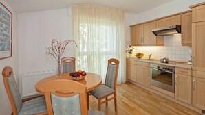 Une cuisine avec des meubles de rangement en bois, une cuisinière et un coin repas comprenant une table et des chaises.