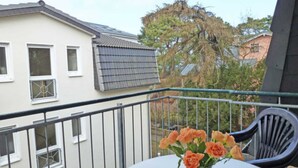 Un balcon avec une table et des chaises, un vase de fleurs et un bâtiment en arrière-plan.