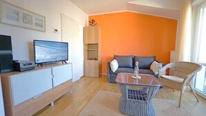 Un salon moderne avec un téléviseur à écran plat, un canapé, un fauteuil en osier et une table basse en verre.