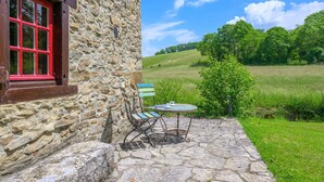 A stone building with a red window and a stone patio with a table and chairs.