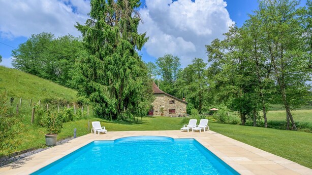 A rectangular swimming pool with two white lounge chairs on one side, surrounded by a stone deck.
