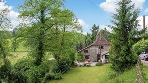 A stone house with a sloped roof, surrounded by lush greenery and a clear sky.