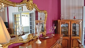 Ein Zimmer mit einem großen, verzierten Spiegel, einer Holzkabine mit Glastüren und einem Tisch mit dekorativen Gegenständen.