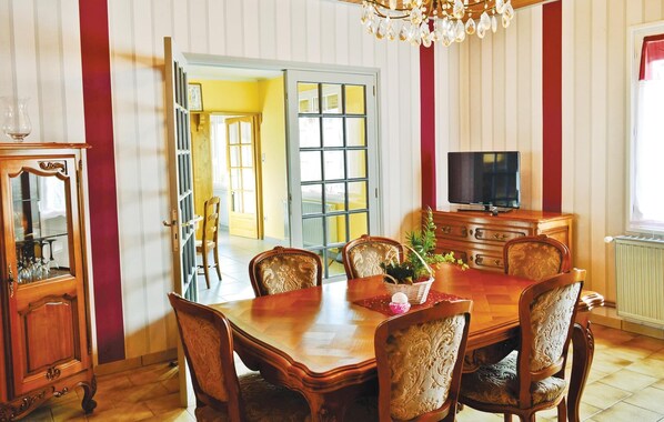 Un comedor con una mesa y sillas de madera, un televisor sobre un mueble bajo y una araña.