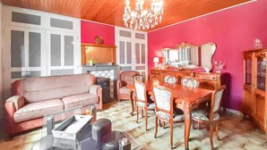 Ein Wohnzimmer mit einem rosafarbenen Sofa, einem Esstisch mit Stühlen, einer Kandelaber und einem Spiegel.