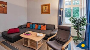 A cozy living room with a sofa, armchair, coffee table, and a large window with curtains. - Villa Malve Whg. 05 - VMa 05 (Heringsdorf)