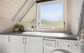 Une cuisine de taille réduite, dotée d’une fenêtre, d’un évier, d’un lave-linge et d’une plante en pot.
