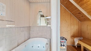 Et træs sauna-rum med et hvidt badekar, en bænk og en saunaovn.