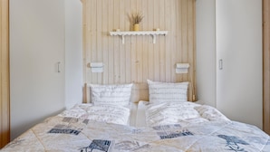 Et soveværelse med bjælke loft, seng med mønstret sengetøj, og en hylde med en vase og stearinlys.