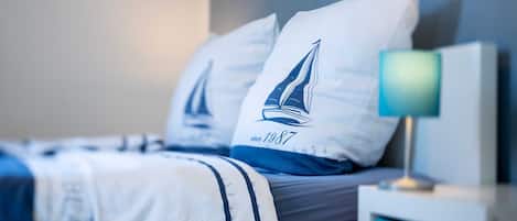 Ein Bett mit Kopfkissen in Segelform, einer Nachttischlampe und einem gerahmten Bild an der Wand.