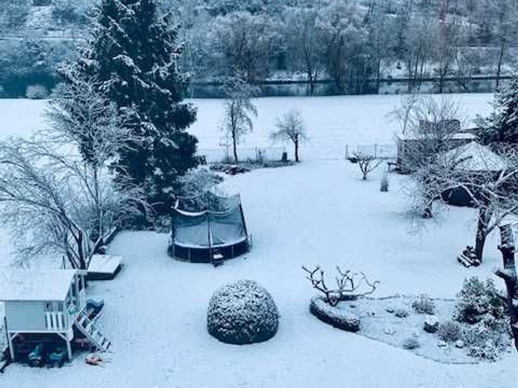 Eine verschneite Außenanlage mit Trampolin, einer kleinen Gartenhütte und einem Baum.
