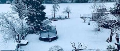 Eine verschneite Außenanlage mit Trampolin, einer kleinen Gartenhütte und einem Baum.