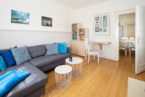 Un salon moderne avec un canapé gris, deux petites tables rondes blanches et un plancher en bois.