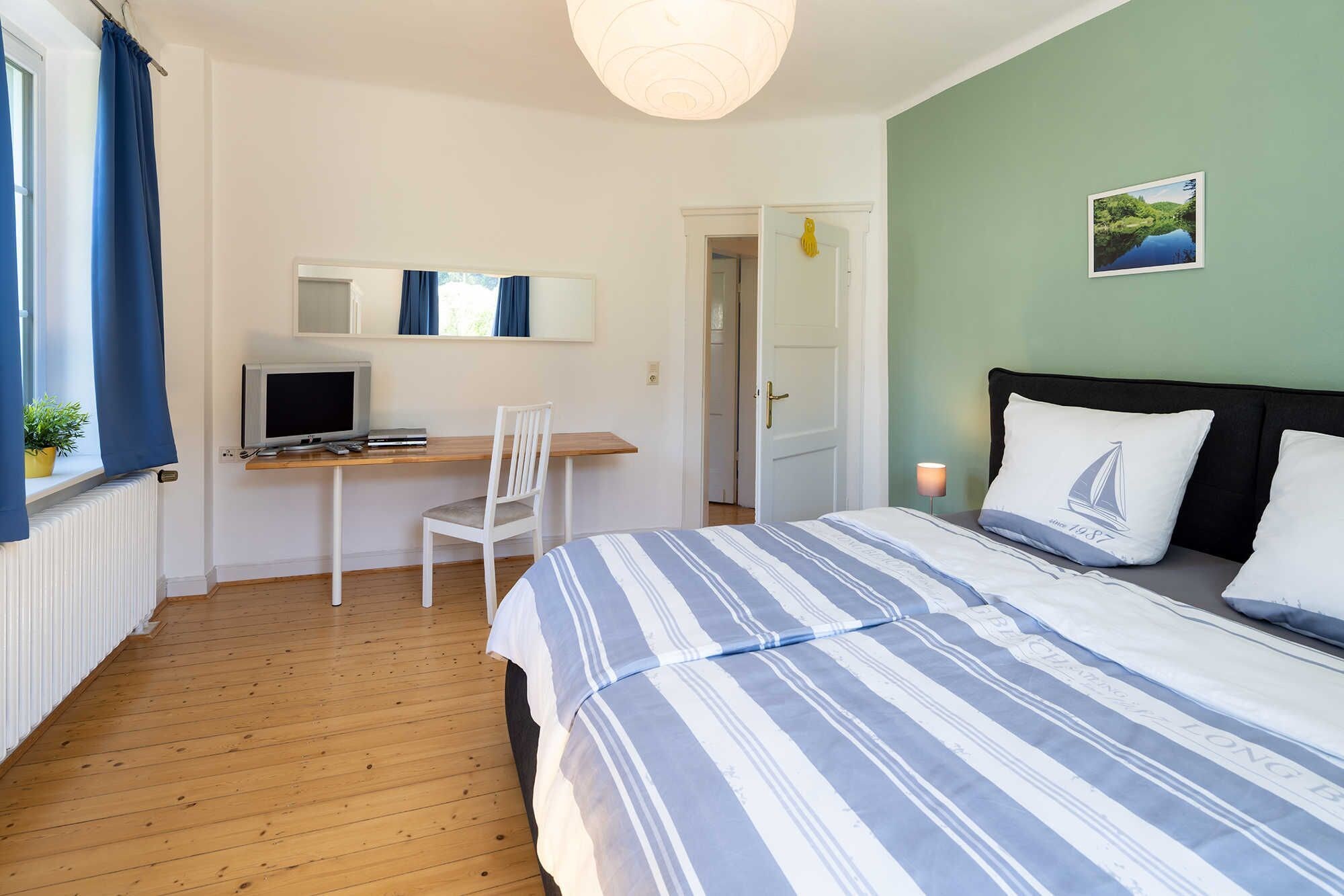 A bedroom with a bed, a desk, a chair, a TV, and a door.