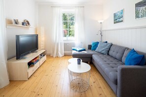 A living room with a television, sofa, coffee table, and a window with curtains.