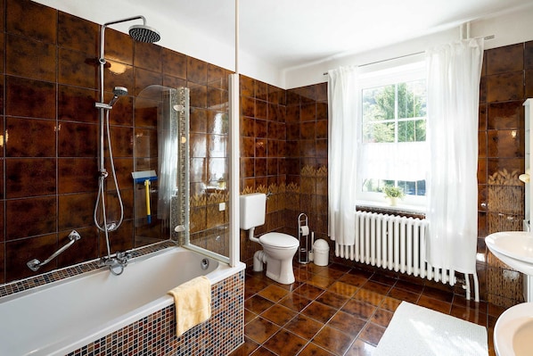 A bathroom with a bathtub, shower, toilet, and a window with curtains.