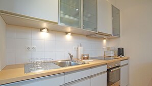 Moderni keittiö, jossa on valkoiset kaapit, ruostumattomasta teräksestä valmistetut kodinkoneet ja puinen työtaso.