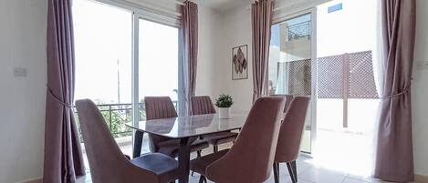 A dining area with a glass table, four chairs, and a potted plant.