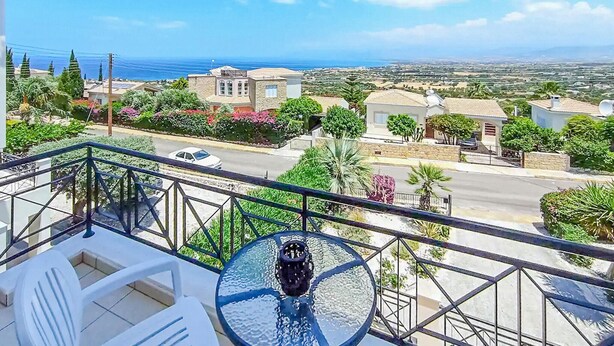 Un balcon doté d’une table et de chaises en verre, donnant sur un quartier résidentiel avec des maisons et offrant une vue sur la mer.