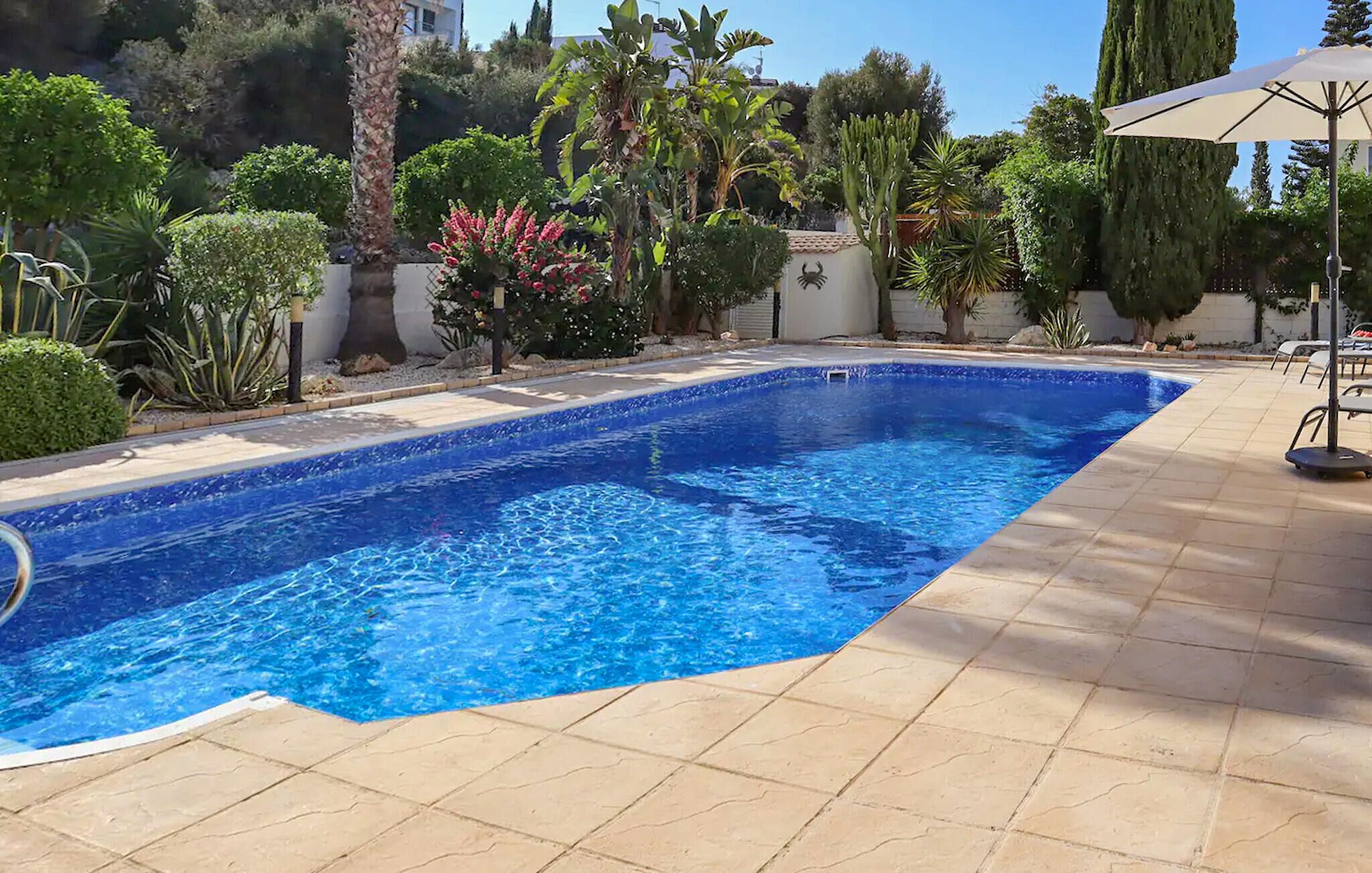 A rectangular swimming pool with clear blue water, surrounded by a tiled patio area.
