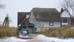 A house with a thatched roof, a boat, and a sandy path leading to it. - Apartment Oystercatcher - beach house bay center (Scharbeutz)