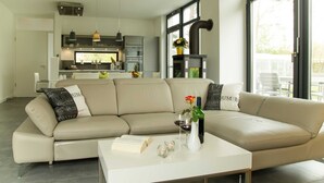 Una sala de estar moderna con un sofá seccional beige, una mesa de centro blanca y una cocina al fondo.