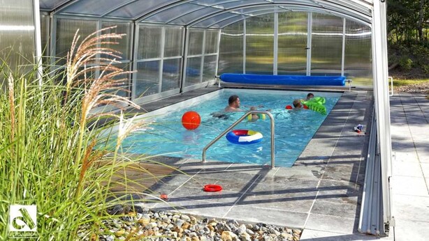 Una piscina cubierta con techo transparente, rodeada de piedras y plantas.