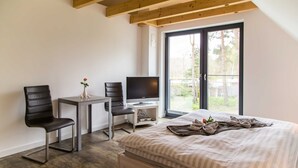 Un dormitorio moderno con cama, dos sillas, una mesita, televisor y ventana con vistas a zonas verdes.