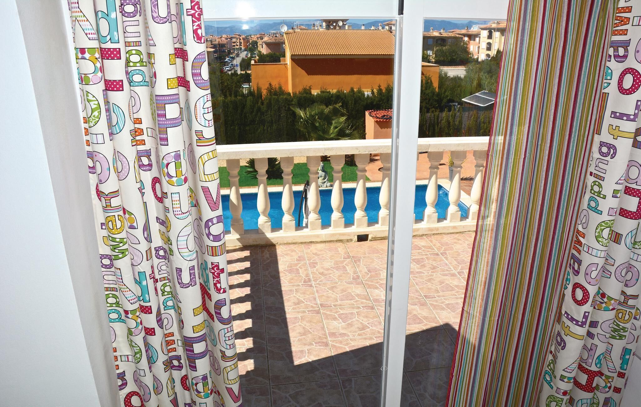 A balcony with patterned curtains, a pool, and a view of buildings.