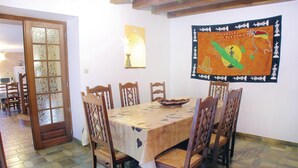Zona pranzo con un tavolo apparecchiato per sei persone, circondato da sedie di legno con sedili imbottiti. Sulla parete è appesa una grande mappa, e si intravede una porta con pannelli di vetro a sinistra.